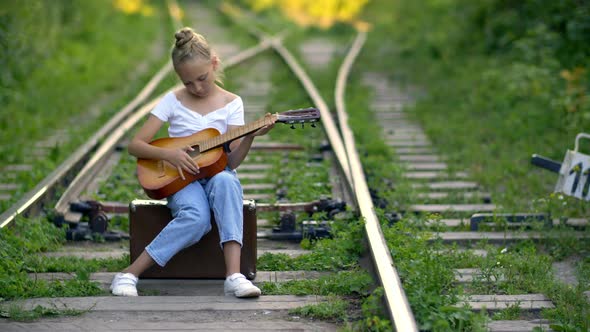 Pensive Girl Sitting on Railroad and Playing Guitar