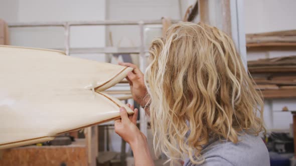 A Caucasian male surfboard maker polishing a wooden surfboard edge