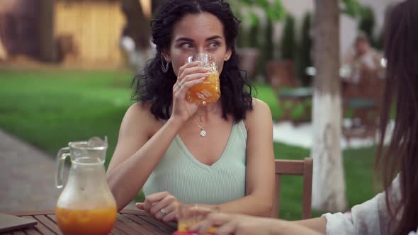 Young Women Drinking Orange Juice and Talking at Outdoor Cafe Smiling Portrait of Brunette Woman