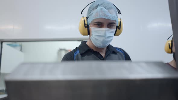 Male Worker In Mask Hairnet And Headphones During Operation In A Beer Factory