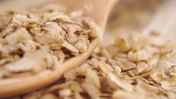 Falling uncooked dry wheat spelt flakes on a wooden spoon. Fall dry cereal in slow motion