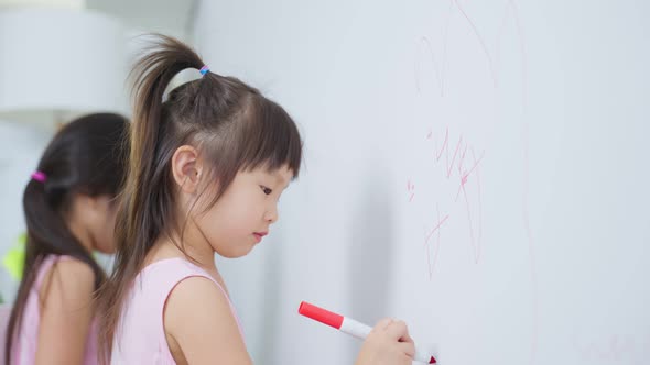 Asian young sibling kid girl enjoy paint on white wall in living room.