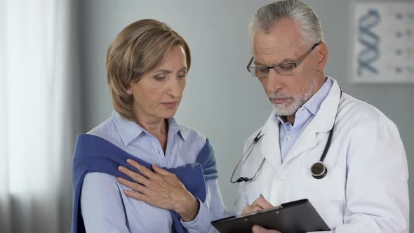 Elderly Doctor Talking to Female Patient Showing Results, Disease, Treatment Way