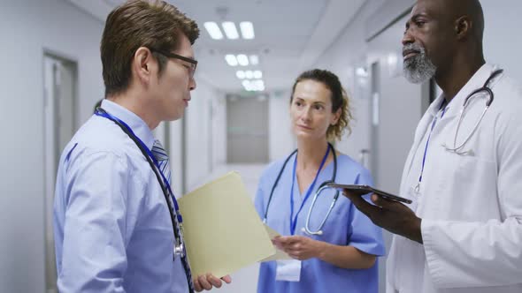 Diverse group of a female and two male doctors talking in hospital corridor holding tablet and files