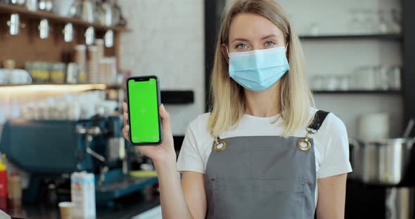 Portrait of Caucasian Woman in Mask Standing Behind Bar and Holding Smartphone with Chroma Key