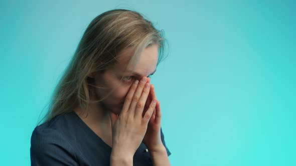 Exhausted Caucasian Surgeon in Her 30s Covering Her Face with Two Palms Over Blue Background