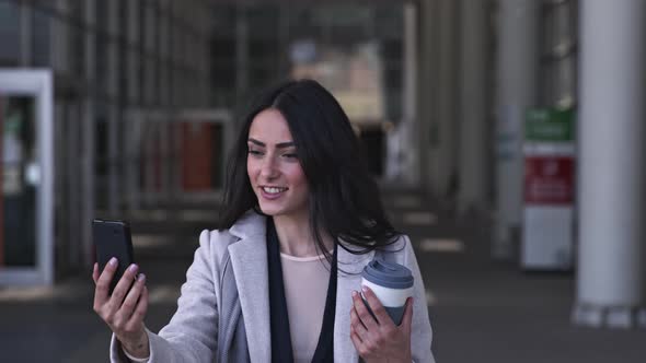 Businesswoman with travel mug, walking in the street with smartphone