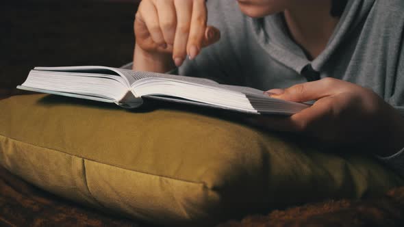 Cute Girl Reads and Leafs Through a Book While Lying Comfortably in Bed