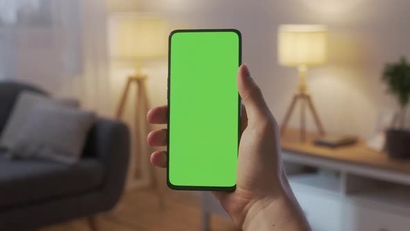 Point of View of Young Man at Home Living Room Using With Green Mockup Screen Smartphone