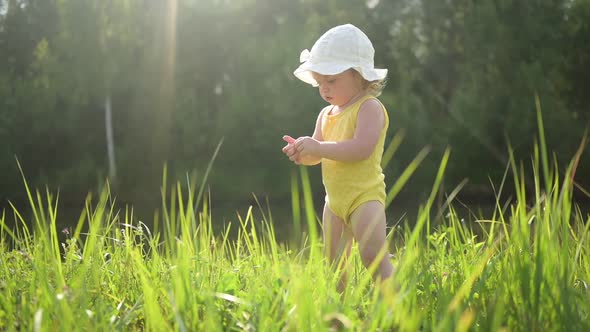 Little Funny Cute Blonde Girl Child Toddler in Yellow Bodysuit and White Hat Walking in Field with