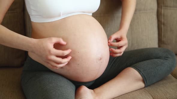 A Pregnant Woman Scratching Her Belly with Her Hand