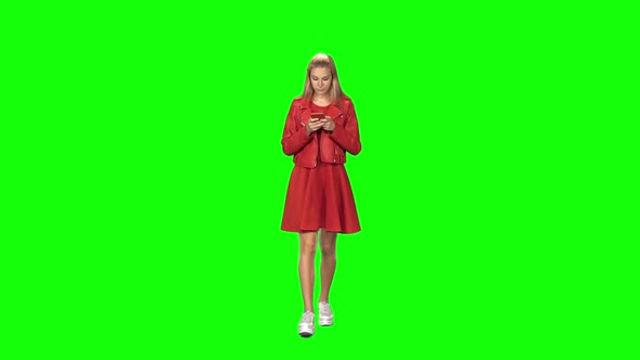 Blonde Girl Is Calmly Walking and Reading Text Message on Her Mobile Phone at Green Screen. Front