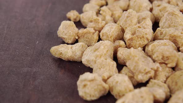 Textured processed soy flakes on a brown rustic wooden surface. Macro