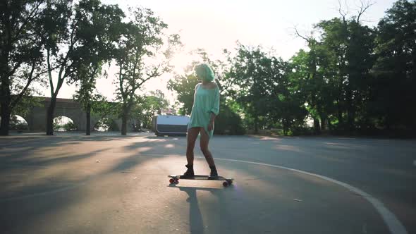 Beautiful Young Girl with Green Hair Riding on Longboard During Sunset Slow Motion