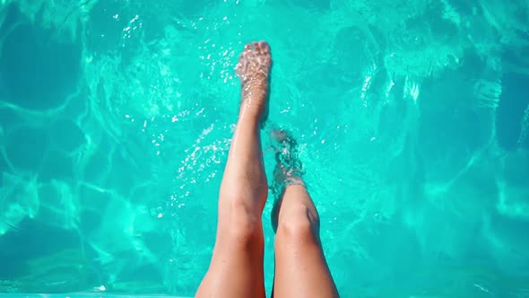 Unrecognizable Slim Female Legs Splash in the Pool on a Hot Summer Day