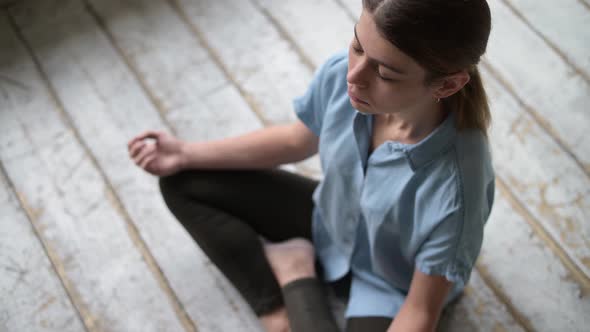 Young woman meditating sitting on the floor in an empty construction apartment