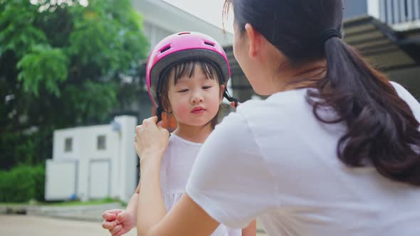 Asian mother put on sport helmet to little kid for safety before exercise ride bicycle on street.