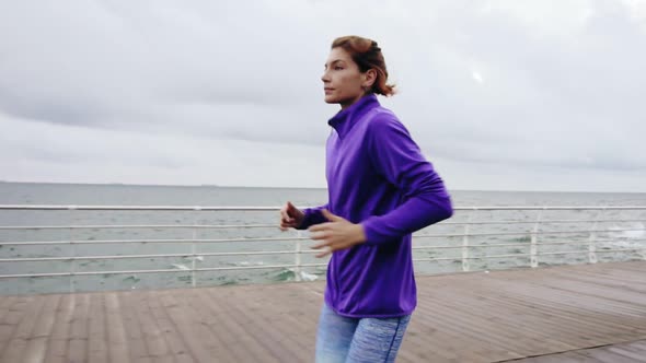 Closeup View of Young Athletic Woman Running Outdoors in Slow Motion on Promenade Near Ocean