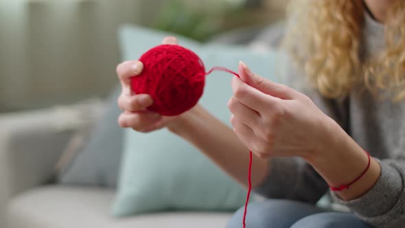 Hands of a Young Girl Wind Up Red Threads for Knitting Into a Ball