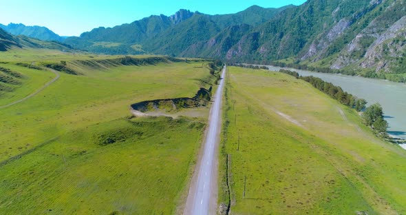 Aerial Rural Mountain Road and Meadow at Sunny Summer Morning. Asphalt Highway and River