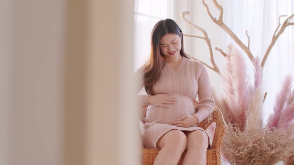 Happy Pregnant Woman sitting on couch holding and stroking her big belly at cozy home