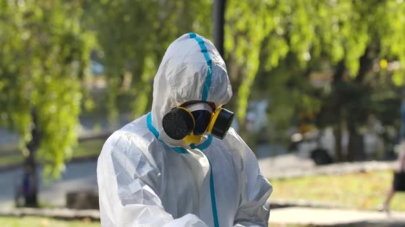 Person of the Disinfector in a Protective Suit Sprays the Disinfectant on the Handrail and Wipes It