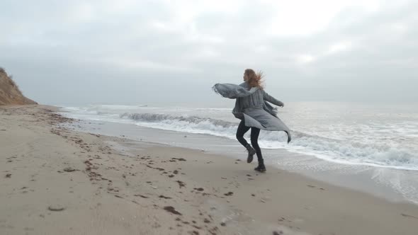 Attractive Redhead Woman in Coat Running on the Wild Autumn Beach