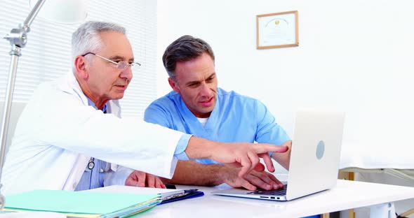 Male doctor and colleague discussing over laptop