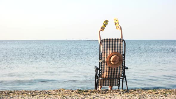 Rear View Woman in Beach Chaise Longue Waving Her Flipflops