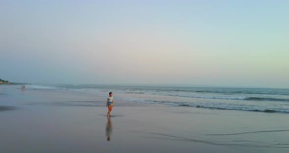 Aerial drone view of a young woman walking on the beach at sunset.