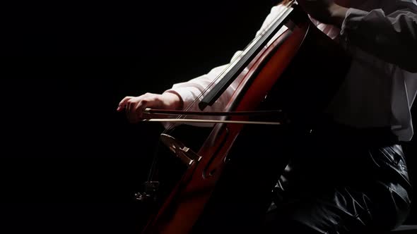 Girl's hand playing cello, closeup on black background. Cello strings and bow closeup, side view.