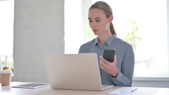 Woman Browsing Internet on Smartphone While Using Laptop in Office