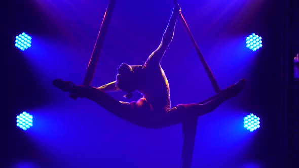 Young Woman Doing Show Acrobatic Trick on Air Silk. Exciting Acrobatic Show in a Dark Studio with