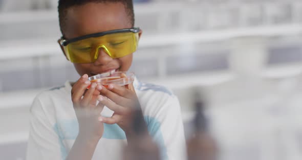 Video of happy african american boy wearing glasses and holding reagent during chemistry lesson