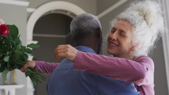 Mixed race senior couple hugging each other in the living room at home