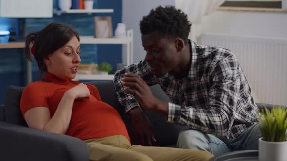 Pregnant Interracial Couple Sitting on Living Room Couch