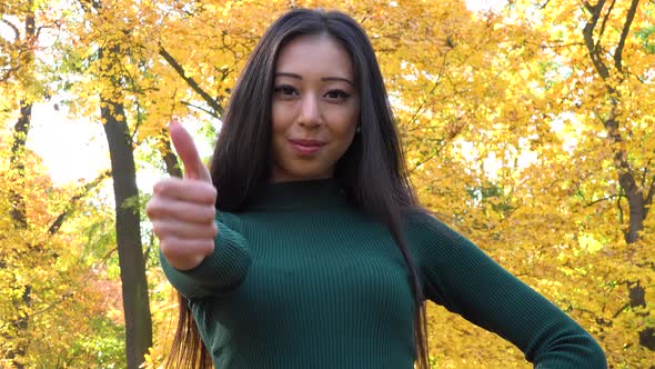 A Young Asian Woman Smiles and Shows a Thumb up To the Camera in A Park