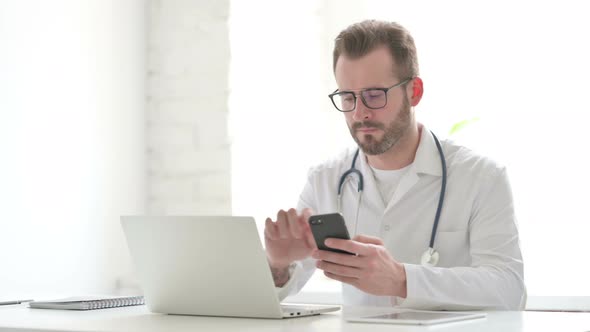 Doctor Using Smartphone While Using Laptop in Office