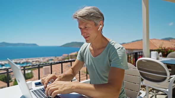 Joyful Man Wearing Headphones Communicating with Friends Via Video Computer Call During Sea Resort