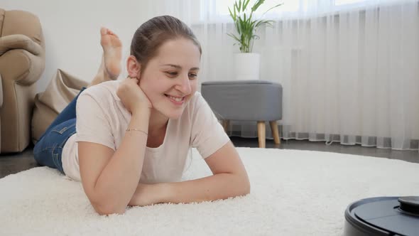 Happy Smiling Woman with Working Robot Vacuum Cleaner on Flooar at Living Room