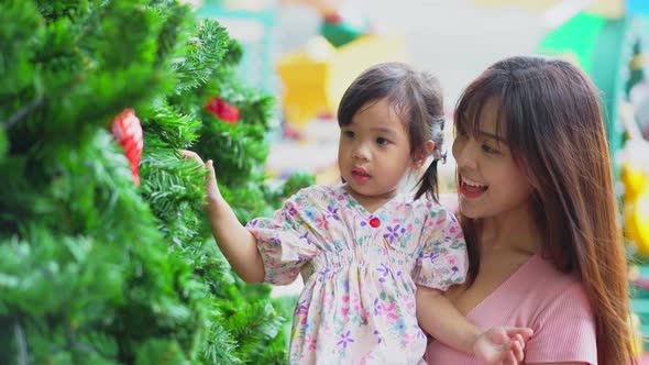 Asian beautiful loving woman carry young daughter on hand play with christmas tree at shopping mall.