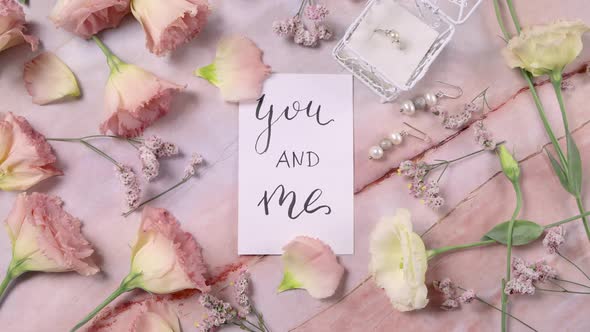 YOU AND ME card on a marble table near pink flowers top view zoom in