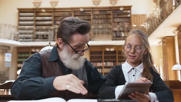 Schoolgirl with Glasses Showing How to Use Ebook to Her Respected Old Bearded Grandpa