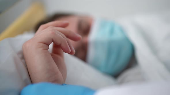 Closeup Hand of Ill Fatigue Caucasian Man in Covid19 Face Mask Lying in Bed with Nurse Palm Helping