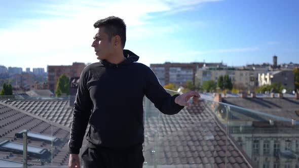 Dolly Shot Portrait of Confident Young Man Walking at Glass Fence on Rooftop Looking Around