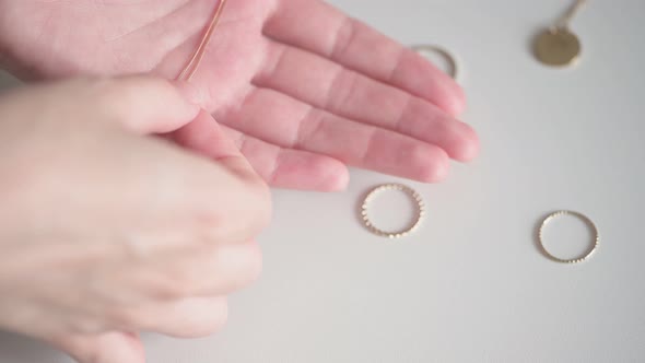 Young woman hands take gold necklace with white precious stone from among rings and jewelry