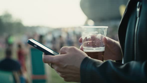 Unrecognizable caucasian man browsing phone on music festival while drinking beer. Shot with RED hel