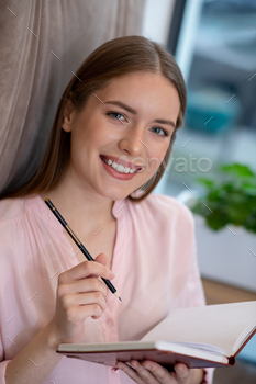 Smiling young and creative woman writing ideas in her notebook / Photodune, Misc