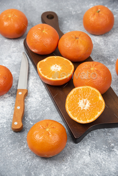 A wooden board full of juicy orange fruits with slices and a knife on stone background / Photodune, Misc