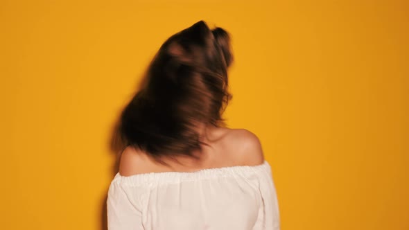 Beautiful smiling cute model shaking her head. Slow motion. Posing in studio near yellow wall 